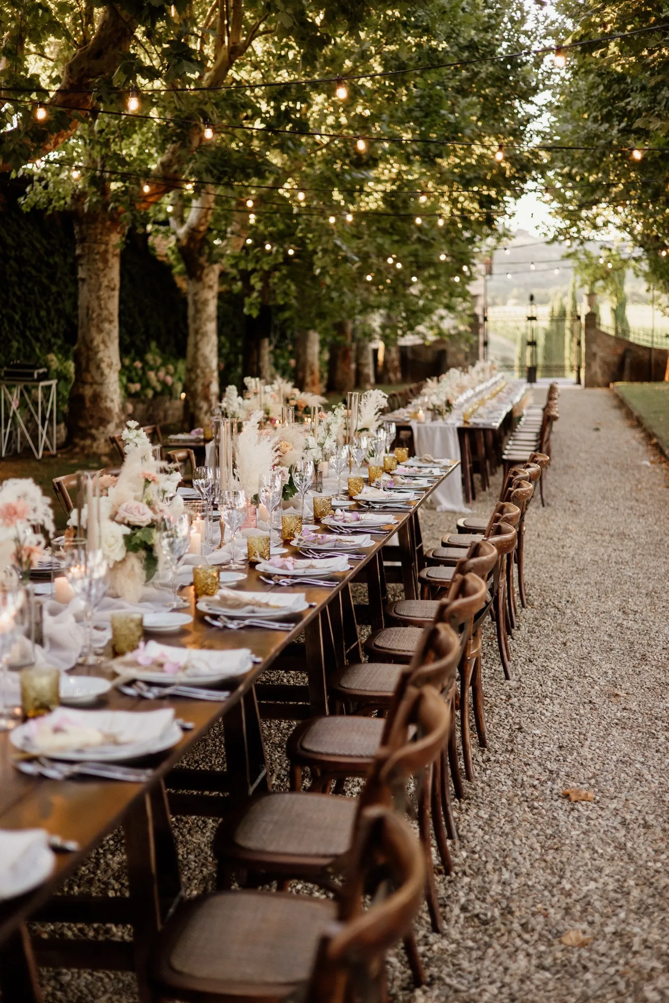 Long wooden table setting with floral arrangements and candlelight, Tuscan villa wedding reception.