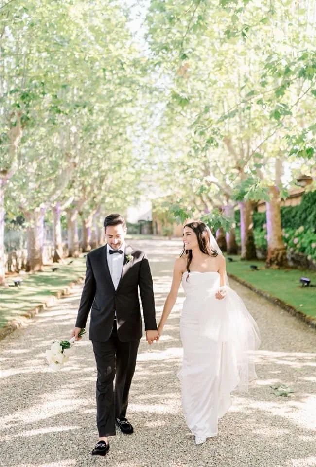Bride and groom holding hands walking down a tree-lined avenue in Tuscany, Italy, luxury destination