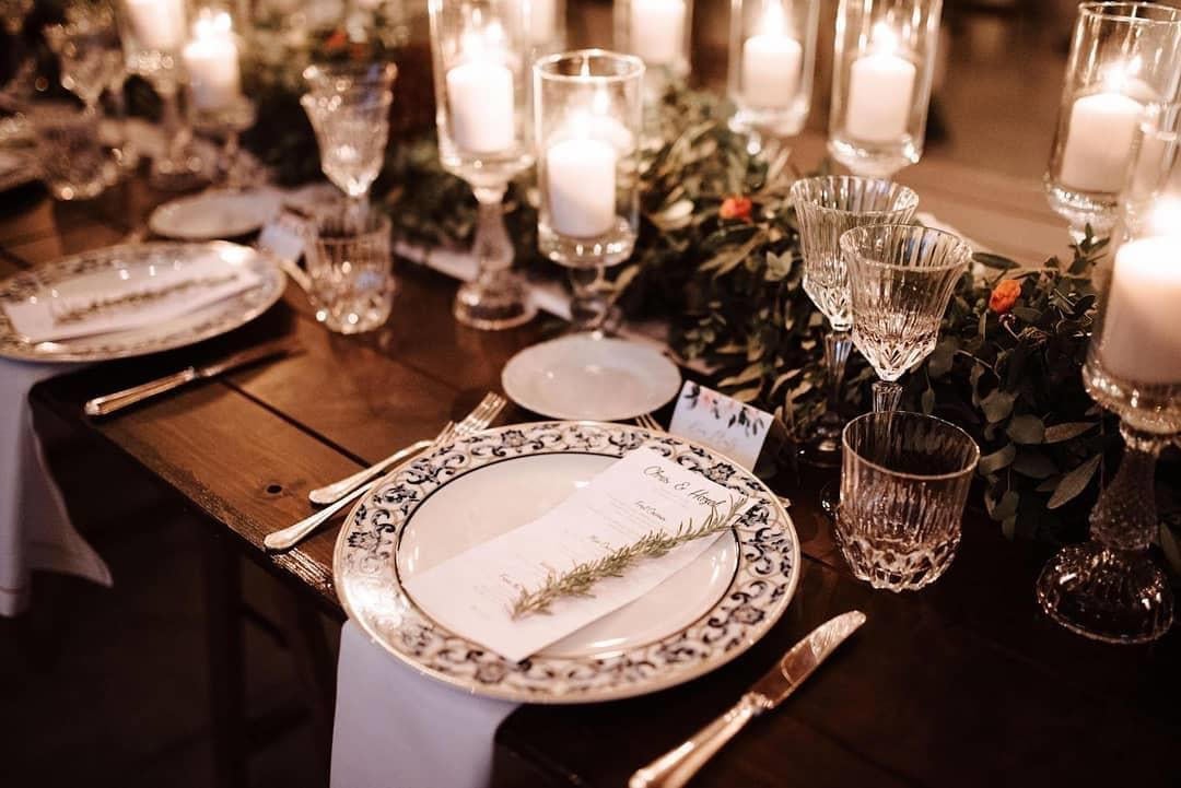 Elegant dining table set with candles, crystal glassware, and decorative greenery